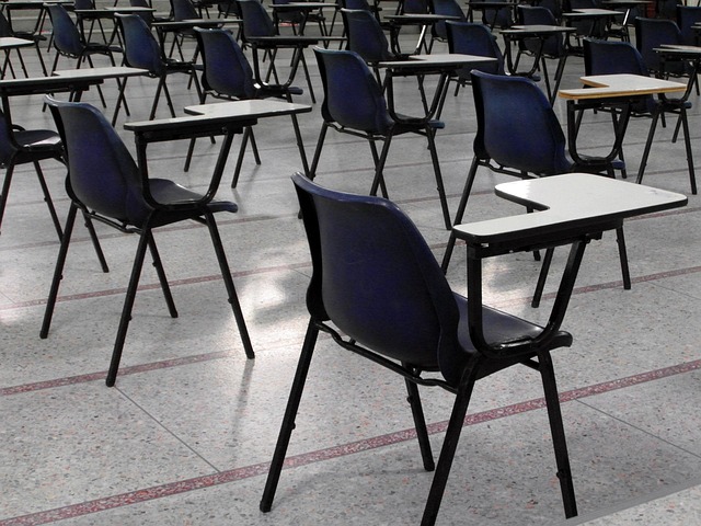 An image showcasing a dimly lit, towering examination hall with rows of empty desks, each equipped with a single pen